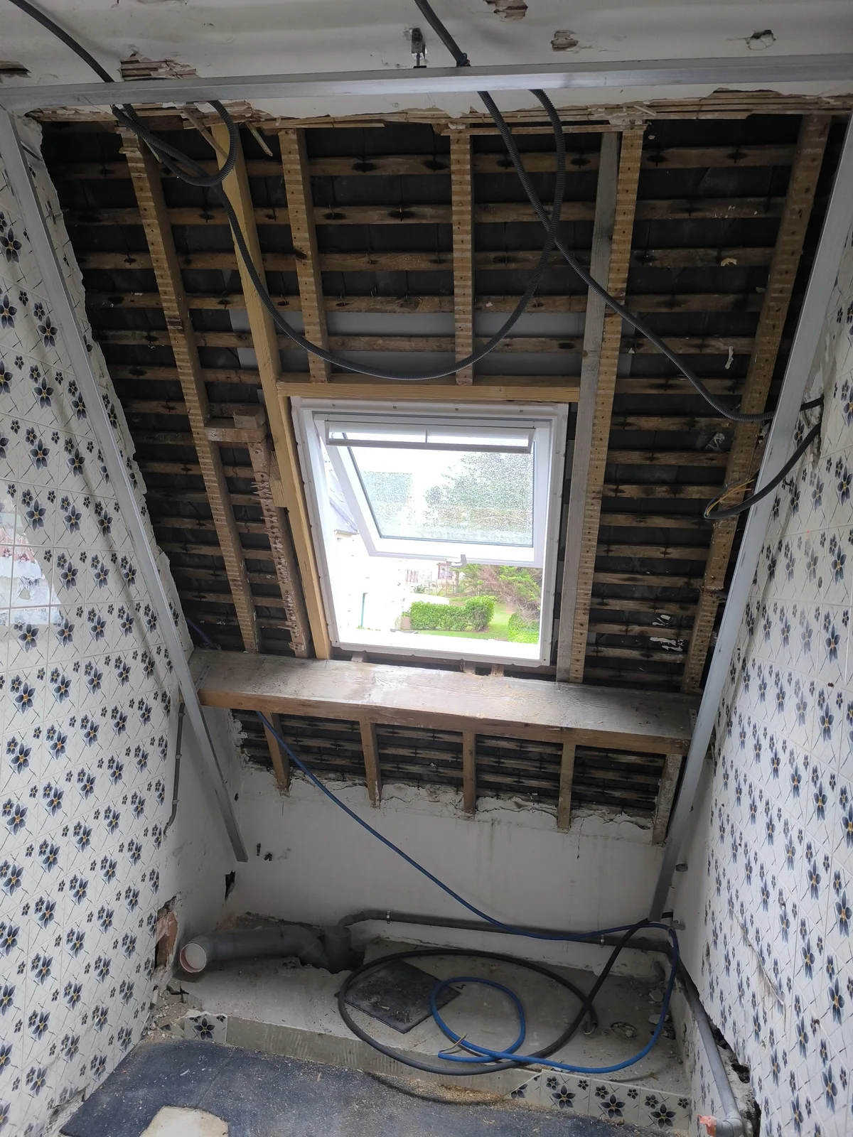 Chantier en cours : le plafond d'une salle de bains déposé, chevrons et liteaux à nu, une fenêtre de toit neuve posée dans son chevêtre de bois clair