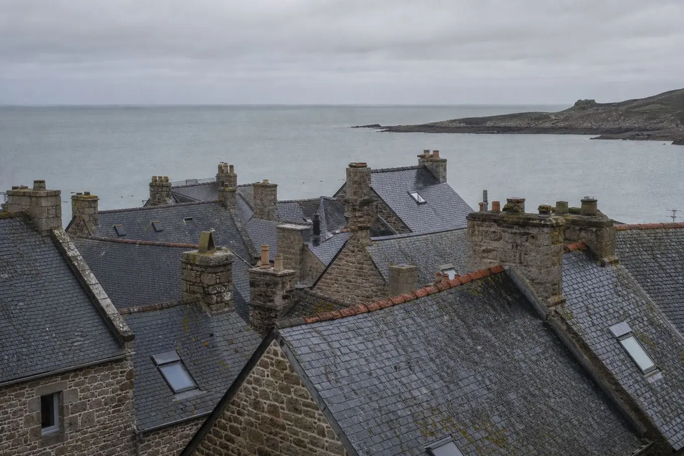 Toitures en ardoise serrées d'un village de bord de mer, souches de granit, la mer grise au fond après une averse